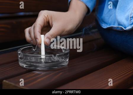 Woman putting out cigarette in ashtray on wooden bench, closeup Stock Photo