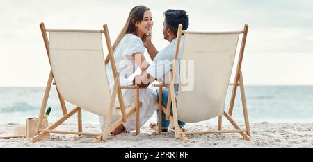 Happy, travel and love of a couple from India on a beach, ocean and sea vacation. Happiness of Indian people smile with a peace, relax and calm mindset together by the waves, sand and water in nature Stock Photo