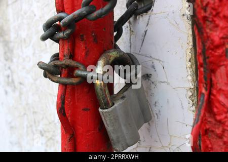 An old padlock on a rusty chain wrapped around red pipes.. Stock Photo