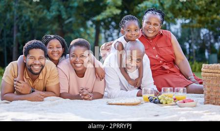 Love, picnic and family time with black people smile and relax at a park or forest, bonding and having fun. Portrait cheerful girl enjoy weekend with grandparents and parents, playing and embracing Stock Photo