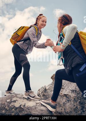 Hiking, help and friends out on a rock or mountain climbing adventure for fitness, exercise and adrenaline. Happy women with support, travel and assistance while out on cliff and reaching the summit Stock Photo