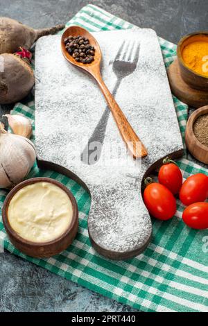 bottom view wooden spoon on chopping board spices in bowls garlic beets cherry tomatoes on grey table Stock Photo