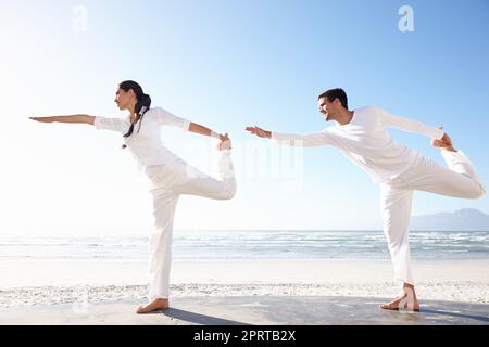 Synchronised beside the sea. Full length shot of a young man and woman doing yoga beside the sea. Stock Photo