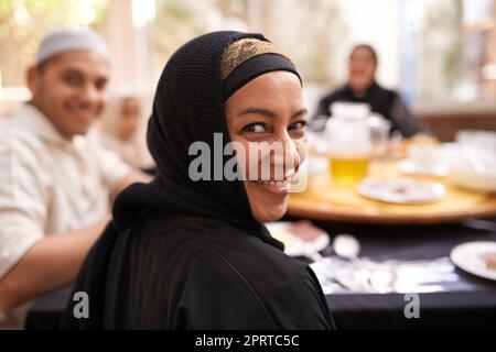 Hope you brought your appetite. Portrait of a muslim woman looking back while eating with her family. Stock Photo