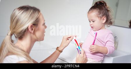 Baby kid brushing teeth with mom in bathroom, morning oral hygiene and clean dental healthcare wellness. Parent with toothpaste and toothbrush teaching young toddler girl child healthy mouth cleaning Stock Photo