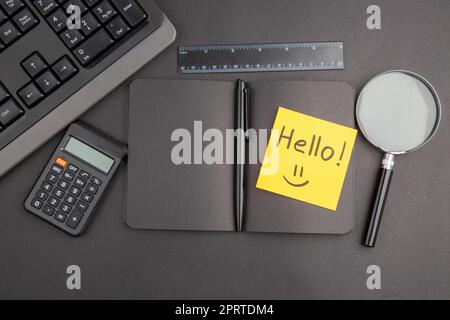 top view black notebook pen keyboard hello written on note paper lupa ruler calculator on dark background Stock Photo