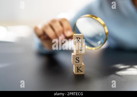 Hand Looking At Risk Blocks Through Magnifying Glass Stock Photo