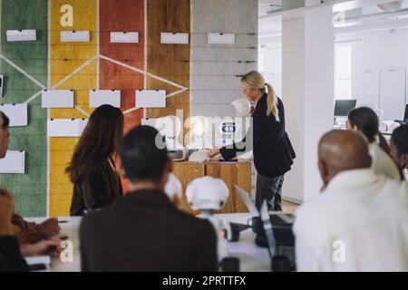 Female professor explaining students over social robot in innovation lab Stock Photo