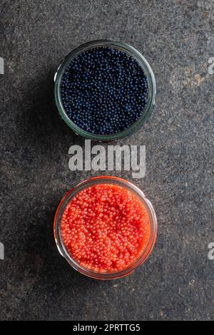Red and black caviar in jar on dark table. Stock Photo