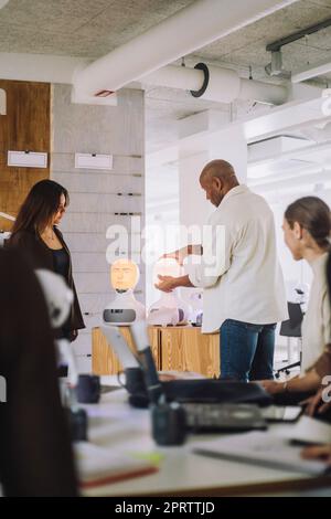 Male professor explaining students over social robot in innovation lab Stock Photo