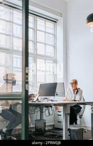 Male and female business people discussing while sitting at desk in office Stock Photo