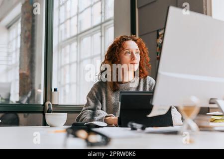 Focused redhead businesswoman working on desktop PC at office Stock Photo