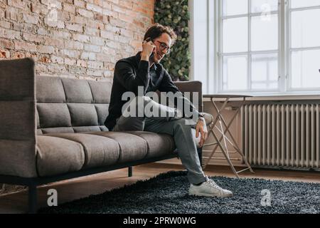 Smiling businessman talking on smart phone while sitting on sofa at office Stock Photo