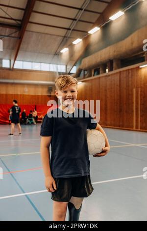 Smiling boy with disability holding soccer ball while standing at sports court Stock Photo