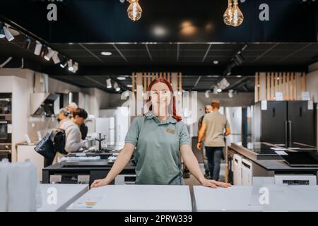 Portrait of smiling female sales clerk leaning on washing machine in electronics store Stock Photo