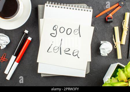 top view cup of tea red and black markers binder clips compasses good idea written on notepad on black background Stock Photo