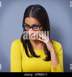 Heres looking at you...Studio portrait of a beautiful young woman peering through her glasses against a blue background. Stock Photo