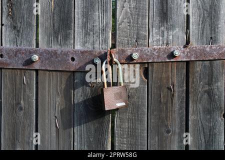 Padlock brown metal lock close-up on old gray wooden gate. Stock Photo