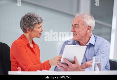 Theyve worked together for a long time. two mature business colleagues sitting with a digital tablet and discussing work. Stock Photo