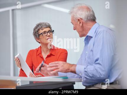 Working on a new business strategy. two mature business colleagues sitting with a digital tablet and discussing work. Stock Photo