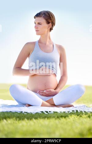 Yoga for two. a beautiful pregnant woman doing yoga outdoors. Stock Photo