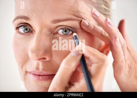 Making her best features stand out. Cropped studio shot of a mature woman applying eyeliner. Stock Photo