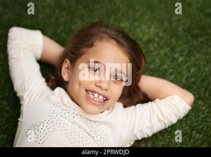 Carefree childhood days. High angle portrait of a cute little girl lying on her back on the grass. Stock Photo