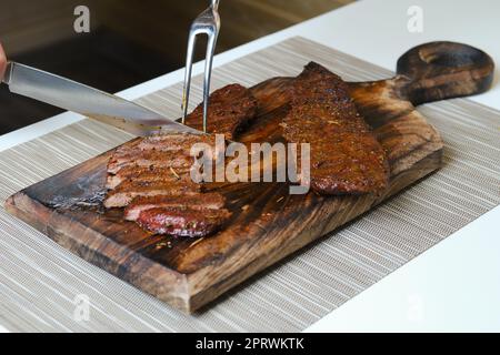 Cutting steak on wooden cutting board with knife and fork Stock Photo