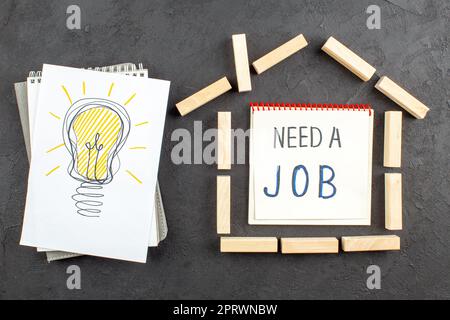 top view idealight bulb drawing on paper house shaped wood blocks need a job written on notebook on black background Stock Photo