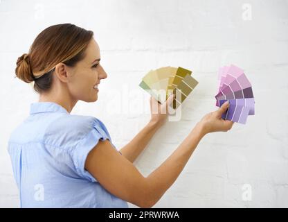 I cant make up my mind. a woman holding up colour swatches uo to the wall. Stock Photo
