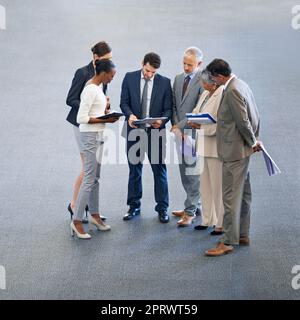 Many heads equals better ideas. High angle shot of a group of businesspeople looking at documents in a lobby. Stock Photo