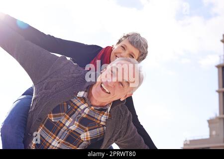 Never stop having fun. Portrait of a happy senior couple enjoying a piggyback ride outdoors. Stock Photo
