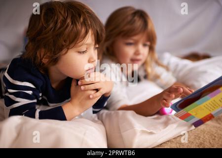 Fairytales under the fort. two adorable siblings using torches to read a book inside their blanket fort. Stock Photo