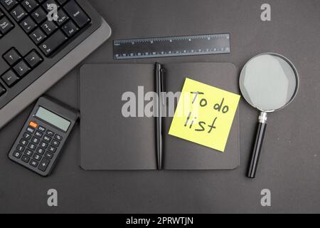 top view black notebook pen keyboard to do list written on note paper lupa ruler calculator on dark background Stock Photo