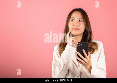 young woman excited smiling holding mobile phone and think idea finger touch face Stock Photo
