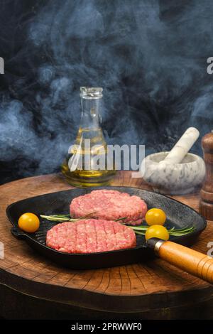 Smoky raw beef burger patty on frying pan Stock Photo