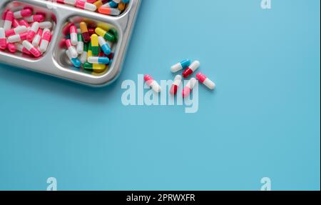 High-angle view of multi-colored antibiotic capsule pills on stainless steel tray and blue background. Antibiotic drug resistance. Prescription drugs. Pharmaceutical industry. Healthcare and medicine. Stock Photo