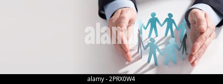 Businessperson's Hand Protecting Paper Cut Out Figures Stock Photo