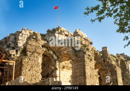 The red Turkish flag flies on top of major ruins of the amphitheatre next to the Temple of Dionysus at Side ancient Roman city in Turkey (Turkiye). Th Stock Photo