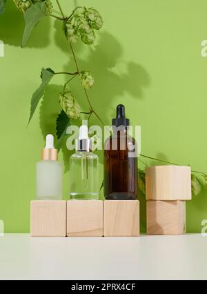 Three glass bottles with pipettes for cosmetics, acids, oils on a green background. Empty containers Stock Photo