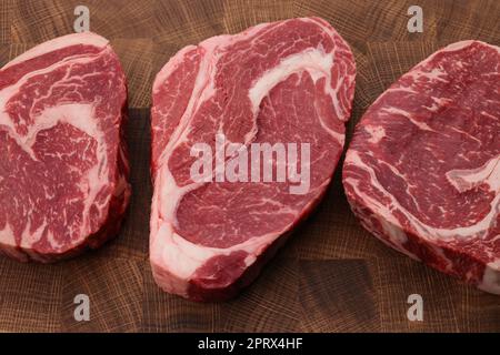 Three raw ribeye beef steaks on cutting board Stock Photo
