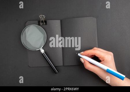 top view lack notepad pen in female hand binder clip lupa on black background Stock Photo
