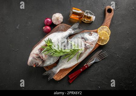 https://l450v.alamy.com/450v/2prx6y2/top-view-raw-sea-fish-on-chopping-board-fork-and-knife-oil-bottle-gralic-onions-on-black-background-2prx6y2.jpg