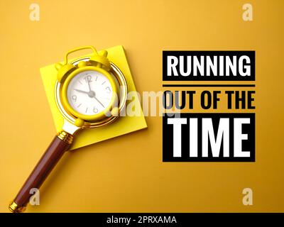 Alarm clock and magnifying glass with the word RUNNING OUT OF THE TIME. Stock Photo