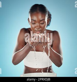 Black woman, water or washing face on blue background in studio for skincare hygiene, healthcare wellness or self care. Beauty model, facial grooming Stock Photo