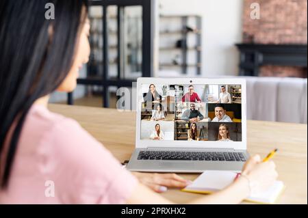 Back view of female employee, team working by group video call share ideas, brainstorming, negotiating use video conference, pc screen view nine multi ethnic young people, comfortable application Stock Photo