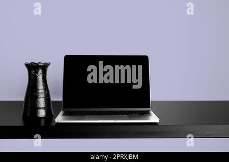 Laptop Mockup on black wooden table with changeable desktop background. Paired with black vase and Purple background. Stock Photo
