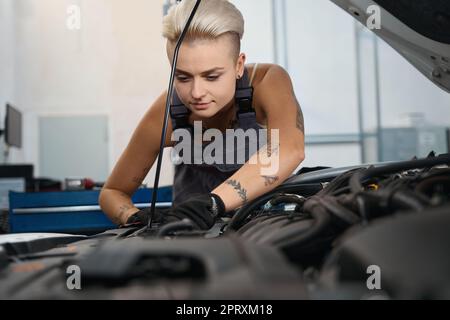 Auto mechanic in work overalls works under hood of car Stock Photo