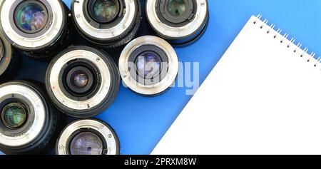 Several photographic lenses and white notebook lie on a bright blue background. Space for text Stock Photo