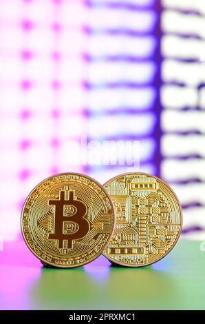 Two gold bitcoins lie on the green surface on the background of the display, which shows the process of mining the crypto currency Stock Photo